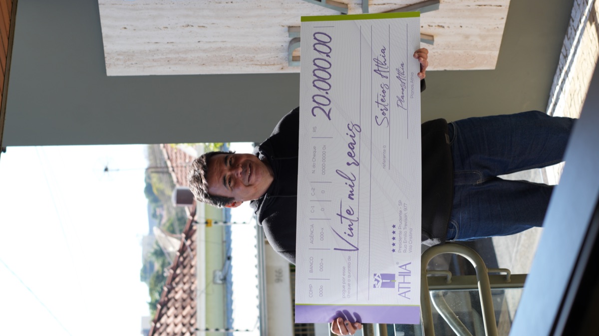 Ganhador do sorteio semanal Athia segurando o cheque